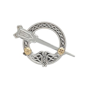 Puede incluir: Un broche celta Claddagh de plata con un corazón dorado y un pasador. El broche está decorado con intrincados nudos y diseños celtas.