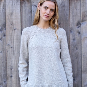 Puede incluir: Un suéter gris claro con cuello redondo y mangas largas. El suéter tiene un tejido de punto texturizado y un ajuste ligeramente holgado.