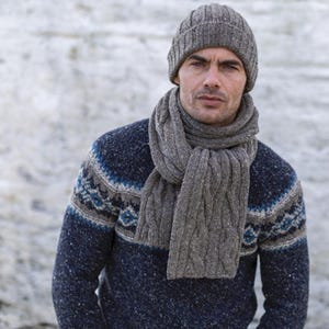 Puede incluir: Un gorro de punto gris y una bufanda a juego. El gorro tiene un borde doblado y la bufanda es de estilo punto de cable.