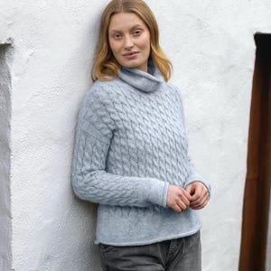 Puede incluir: Un suéter de punto de cable azul claro con cuello alto.