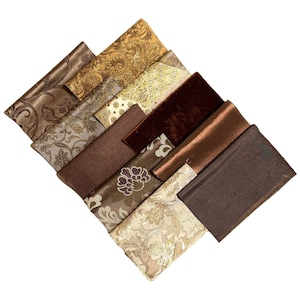 Könnte beinhalten: Sortiment von Stoffproben in verschiedenen Brauntönen und Goldtönen. Die Stoffe haben unterschiedliche Texturen, darunter Samt, Satin und Brokat.