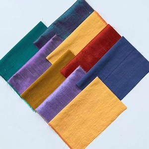 Könnte beinhalten: Eine Sammlung rechteckiger Stoffmuster, die in einem diagonalen Muster angeordnet sind. Die Farben umfassen tiefes Türkis, schillerndes Violett, Goldgelb, leuchtendes Rot, Marineblau, Senfgelb und helles Violett, alle mit einer Webstruktur.