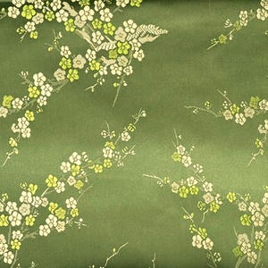 May include: Green fabric with a repeating pattern of white and yellow floral branches. The flowers have a detailed, textured appearance, and the background is a solid, muted green.