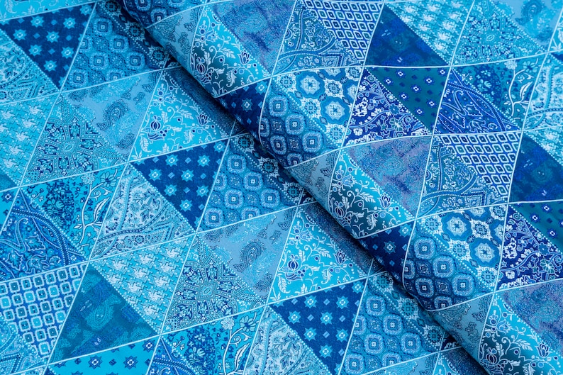 Op de afbeelding: Close-up van een stof met een patchwork-ontwerp in blauwtinten. De stof is verdeeld in driehoekige secties, elk met een ander patroon, waaronder paisley en geometrische motieven. Het algehele effect is een levendig, gestructureerd oppervlak.