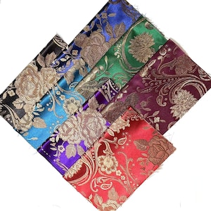 Può includere: Assortimento di campioni di tessuto satinato in vari colori, tra cui nero, blu, verde, viola e rosso. Ogni campione presenta un motivo floreale dorato. I tessuti sono disposti a forma di diamante, mostrando i diversi colori e le trame.