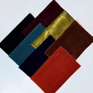 May include: A selection of velvet fabric swatches in a range of colours, including black, teal, navy, gold, brown, and rust. The swatches are arranged in a diamond shape, highlighting the texture and colour variations of the fabric.