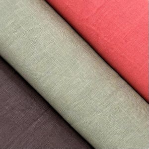 Puede incluir: Primer plano de tres rollos de tela en tonos rojo, verde y marrón. La tela tiene un aspecto texturizado, similar al lino. Los colores son vibrantes y la tela parece estar densamente tejida.