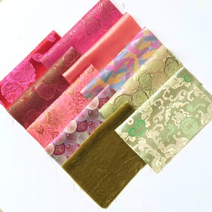 May include: A collection of colorful fabric swatches arranged diagonally. The fabrics display various patterns, including floral, geometric, and abstract designs. Colors range from red and pink to green and gold. The textures vary from smooth to textured.