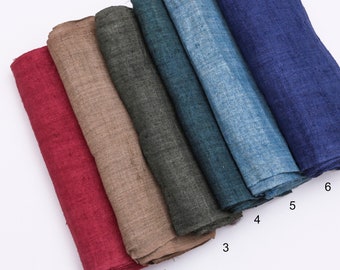 Könnte beinhalten: Eine Sammlung von sechs gefalteten Stoffmustern in verschiedenen Farben. Die Farben umfassen tiefes Rot, Beige, Dunkelgrau, Türkis, Hellblau und Marineblau. Der Stoff scheint Leinen oder ein ähnliches gewebtes Material zu sein.