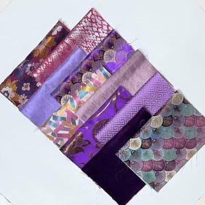 May include: An assortment of fabric swatches in various shades of purple, pink, and gold. The fabrics feature diverse patterns, including floral, geometric, and textured designs. The swatches are arranged diagonally on a white surface.