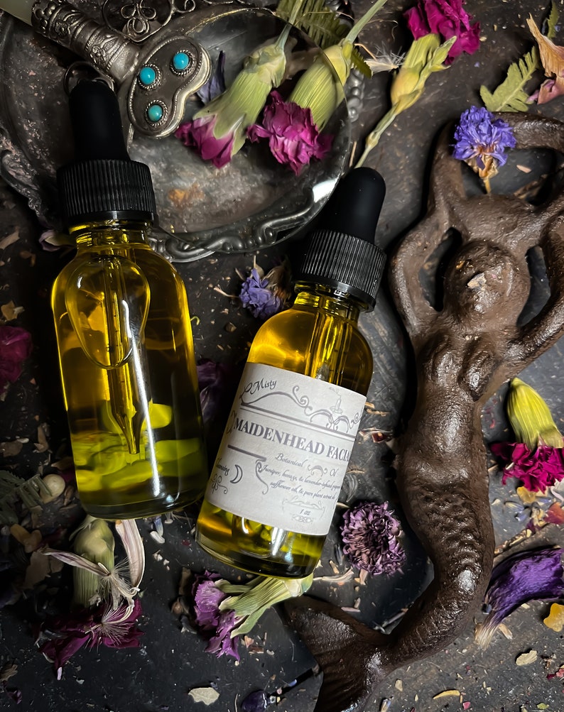Puede incluir: Dos botellas de vidrio &aacute;mbar con goteros, llenas de un l&iacute;quido dorado. Las botellas est&aacute;n etiquetadas con "Maidenhead Facial" y una lista de ingredientes bot&aacute;nicos. Las botellas est&aacute;n rodeadas de flores secas y una figura de sirena de metal.
