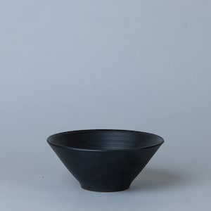 May include: A black ceramic bowl with a wide, shallow opening and a rounded bottom. The bowl has a smooth, glossy finish.