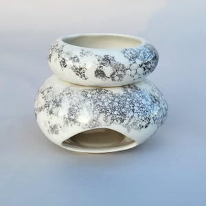 Op de afbeelding: Een tweedelige keramische etherische olieverspreider. De witte stukken hebben een gespikkeld zwart-grijs patroon. Het onderste stuk heeft een grote opening. Het bovenste stuk is een kleine kom die bovenop het onderste stuk zit.