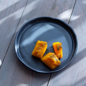 Peut inclure: Trois morceaux de tarte à la citrouille jaune sur une assiette noire. L'assiette est posée sur une surface en bois gris.