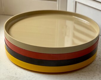 May include: Set of four round plastic trays in yellow, black, red, and beige.