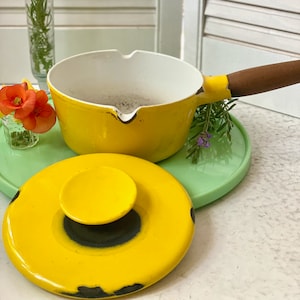 May include: A yellow enamel cast iron saucepan with a wooden handle and a matching yellow lid. The lid has a black knob in the centre.