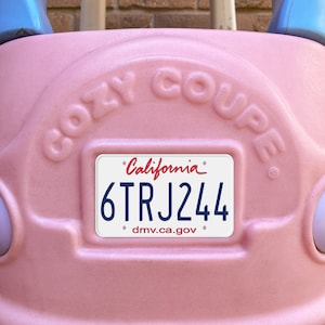 Puede incluir: Coche de juguete de plástico rosa con una matrícula que dice "California 6TRJ244 dmv.ca.gov". El coche tiene las palabras "Cozy Coupe" en relieve en la parte superior.