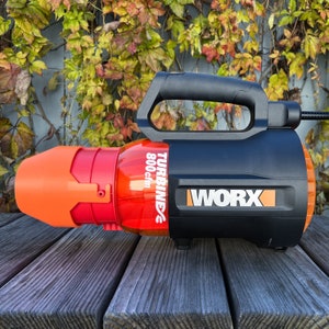 May include: A black and orange Worx Turbine 800 CFM leaf blower with a red and orange nozzle. The blower is on a wooden surface.