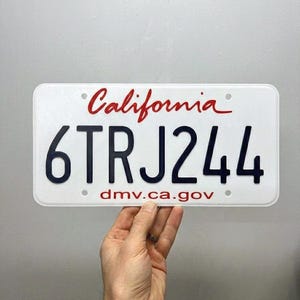 Può includere: Una targa bianca della California con scritte nere e il nome dello stato in corsivo rosso. La targa recita "6TRJ244" e include il sito web "dmv.ca.gov".