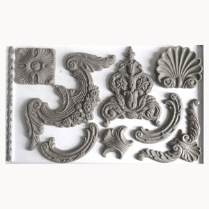 May include: A set of 12 gray silicone molds for making decorative cake toppers or other crafts. The molds feature various ornate designs, including scrolls, flowers, and shells.
