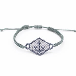 Könnte beinhalten: Handgefertigtes Armband mit rautenförmigem Mittelstück und Anker-Design. Das Armband besteht aus grauem Makramee-Band und ist verstellbar. Das Anker-Design verwendet Grau- und Weißtöne. Die Länge des Armbands ist verstellbar.