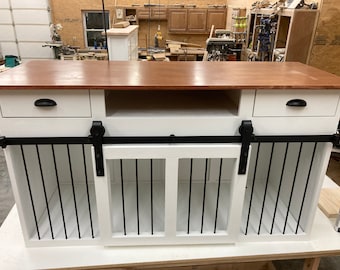 May include: White wooden dog crate with two sliding doors and a top surface. The crate has two drawers and a shelf. The crate is made of wood and has a black metal frame.