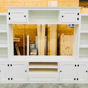 May include: White entertainment unit with a large open space for a television, two cupboards with doors on each side, and two shelves on each end.
