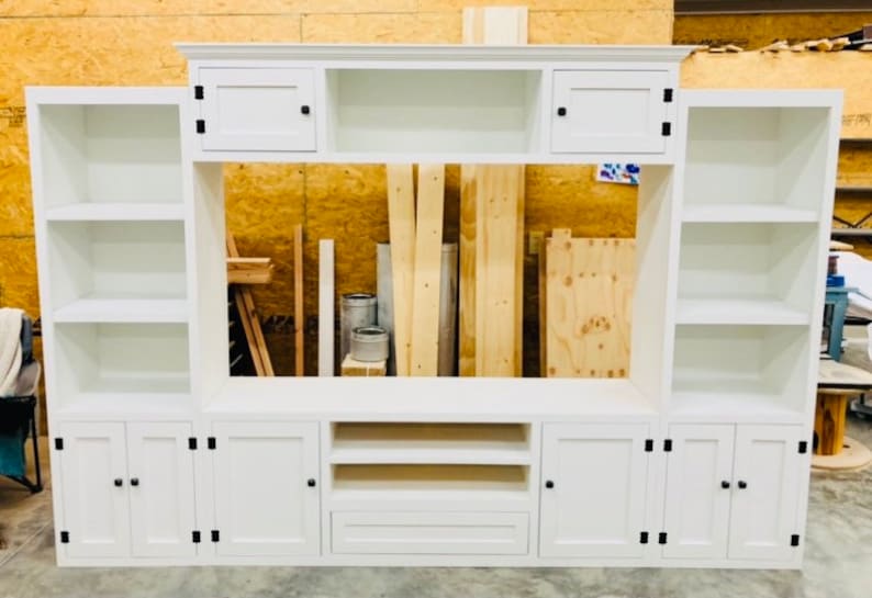 May include: White entertainment unit with a large open space for a television, two cupboards with doors on each side, and two shelves on each end.