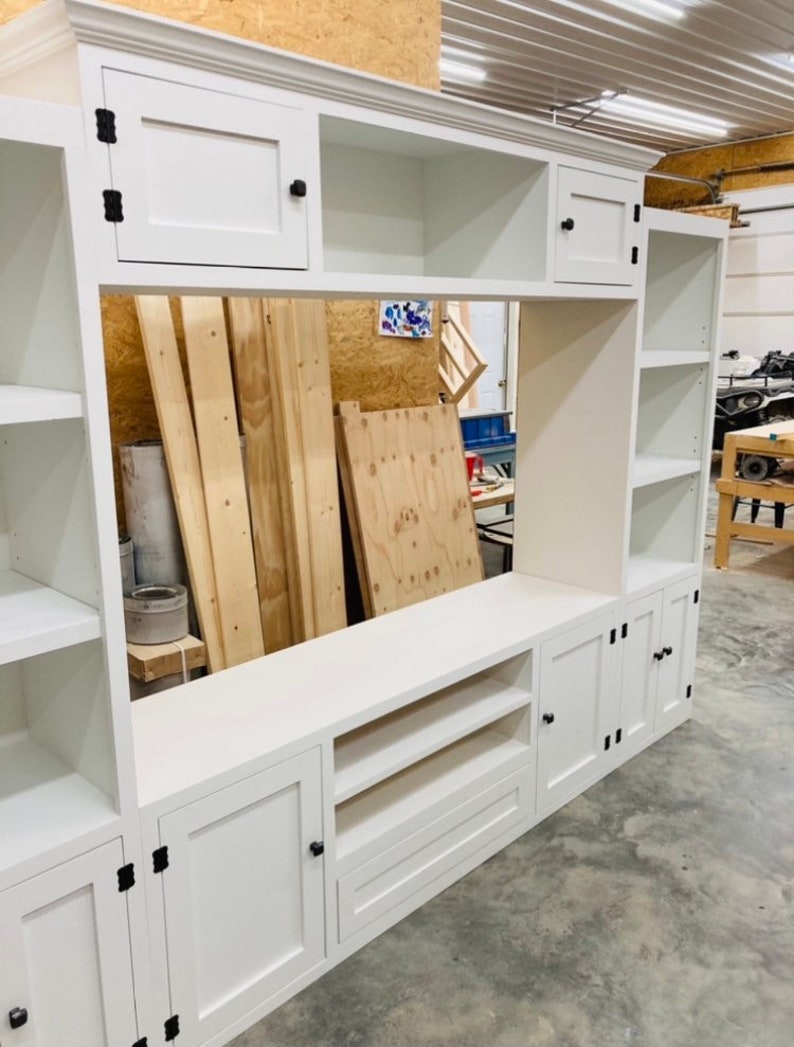 May include: White entertainment unit with open shelves, closed cabinets, and a drawer. The unit has black hardware and is made of wood.