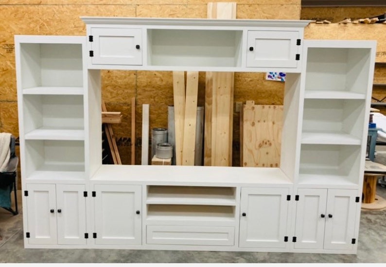May include: White entertainment unit with a built-in shelf, two cupboards, and a drawer. The unit has a white painted finish and black hardware.
