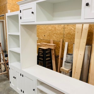May include: White entertainment unit with shelves, cabinets, and drawers. The unit has black hardware and is made of wood.
