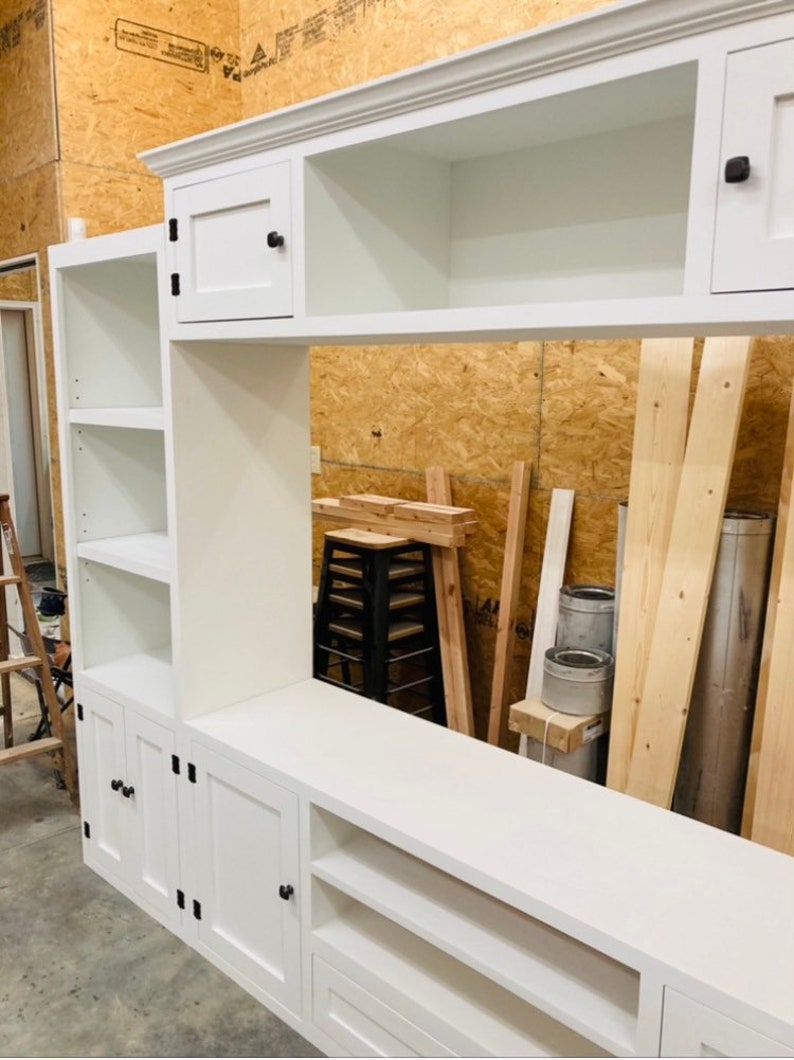 May include: White entertainment unit with shelves, cabinets, and drawers. The unit has black hardware and is made of wood.