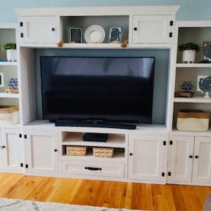 May include: White entertainment unit with a large flat screen TV, shelves, and cupboards. The unit has a white painted finish with black hardware.