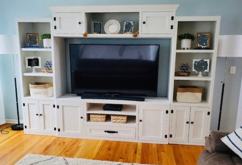 May include: White entertainment unit with a large flat screen TV, shelves, and cupboards. The unit has a white painted finish with black hardware.
