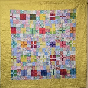 Puede incluir: Una colcha amarilla con un diseño de patchwork que presenta una variedad de patrones florales y geométricos en tonos de rosa, azul, verde y rojo.