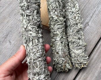 Puede incluir: Tres manojos de salvia blanca, atados con cuerda, sobre una superficie de madera. 