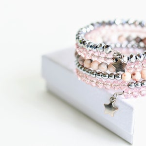 May include: A multi-strand bracelet with pink and silver beads and a star charm. The bracelet is on a white box.