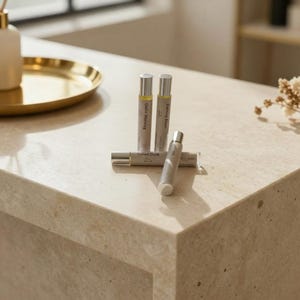 May include: Four small, silver-capped perfume bottles are arranged on a light-colored surface. Two bottles stand upright, while two others are lying down. The bottles are labeled with text, including "Quiet Morning" and "Velvet Dusk."