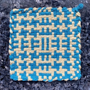 May include: A blue and cream woven pot holder with a geometric pattern. The pot holder has a loop for hanging.