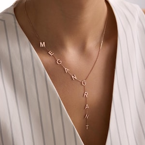 May include: A rose gold necklace with the name "MEGAN GRANT" spelled out in individual letters. The necklace is worn around the neck and hangs down the chest. The letters are connected by a delicate chain.