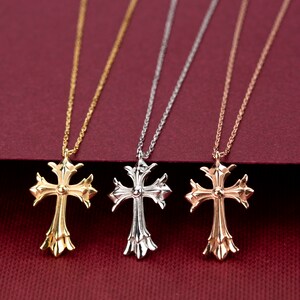 May include: Three gold, silver, and rose gold necklaces with ornate cross pendants. The necklaces are displayed on a red background.