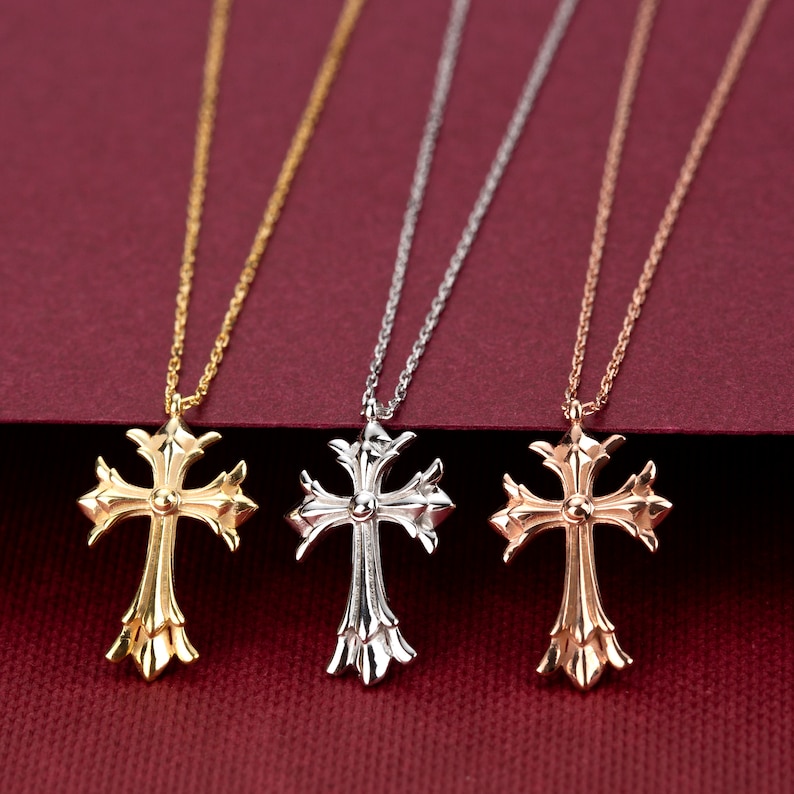 May include: Three gold, silver, and rose gold necklaces with ornate cross pendants. The necklaces are displayed on a red background.