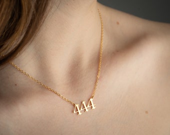 May include: A gold chain necklace with a pendant featuring the number 444 in a gothic font.