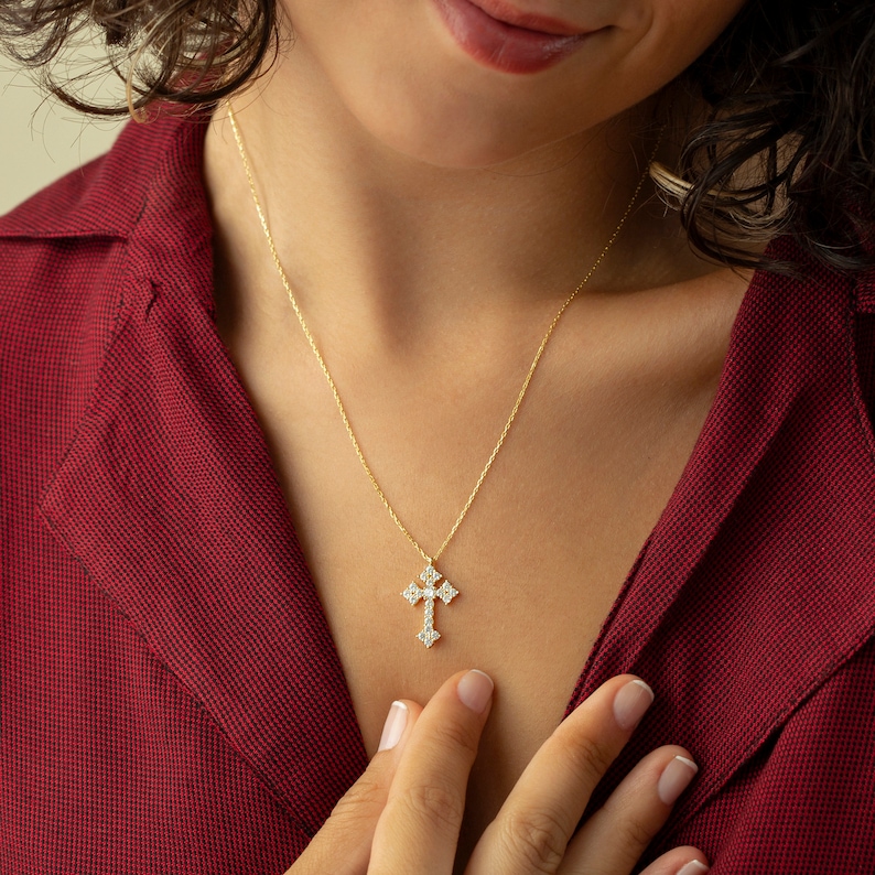 May include: A gold chain necklace with a small, ornate cross pendant. The cross is set with clear cubic zirconia stones.