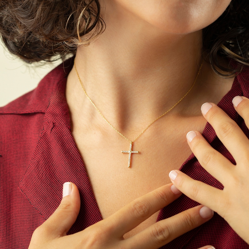 May include: A gold chain necklace with a small, diamond-encrusted cross pendant.