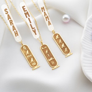 May include: Three gold necklaces with pendants featuring the Egyptian hieroglyphics for "Sarah", "Emily", and "Mama". Each pendant is a rectangular shape with a gold chain.