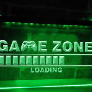 Może przedstawiać: Zielony, podświetlany znak z napisem "GAME ZONE" i ikoną kontrolera. Poniżej znajduje się pasek ładowania z napisem "LOADING". Znak emituje jasne, zielone światło.