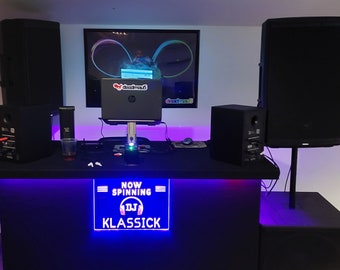 May include: A DJ setup with a laptop, mixer, and two large black speakers. The DJ booth has a blue light strip and a sign that says "NOW SPINNING DJ KLASSICK".