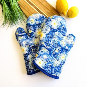 May include: A pair of blue oven mitts with a swirling, starry night design. The mitts feature a vibrant print with white and yellow accents, and a dark blue trim. Kitchen accessories.