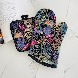 May include: Black oven mitt and pot holder set with a tarot card design. The mitt and pot holder feature colorful illustrations of tarot cards, spiders, and skulls. The text "THE STAR" and "SEVEN OF BONDS" are visible on the cards.